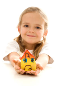 Dziewczynka trzymajaca mały domek na wyciągniętych przed siebie rękach