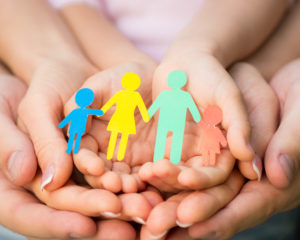 ręce trójki osób, w tym jedne dziecięce trzymające wyciete z papieru postacie rodziców i dzieci trzymajacych sie za rękę